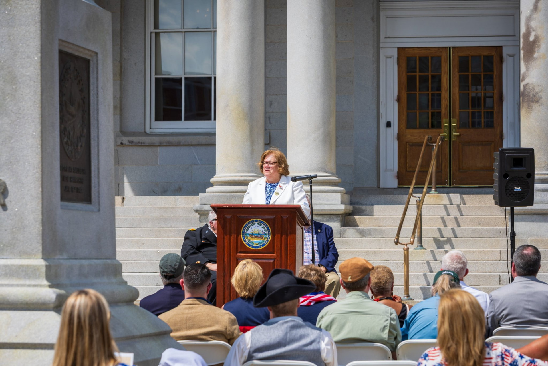 Sharon Carson delivering remarks at an outdoor ceremony on granite steps