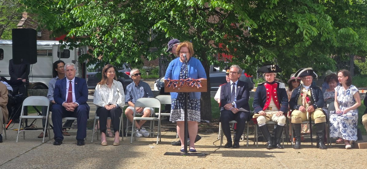 Sharon Carson speaking at an outdoor memorial ceremony with seated guests