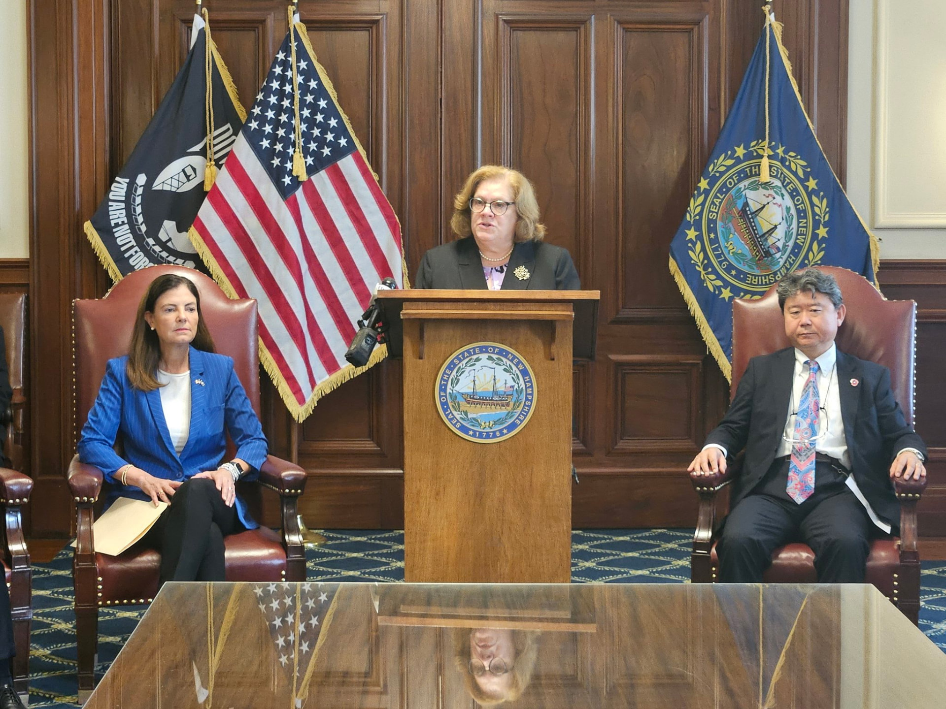 Sharon Carson speaking at a podium alongside state officials at a press conference