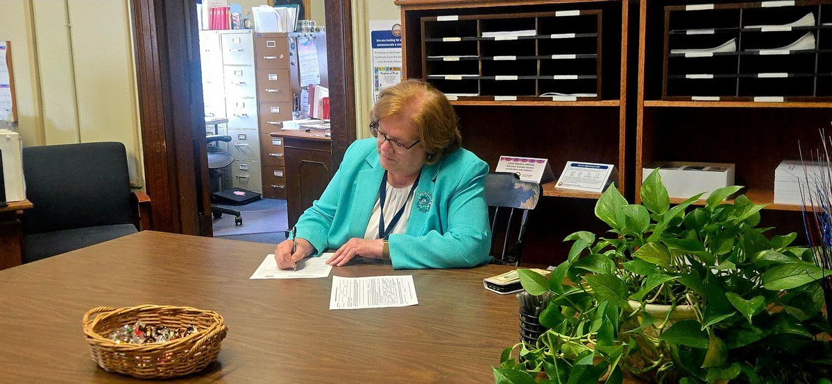 Sharon Carson signing paperwork at a desk in a constituent services office